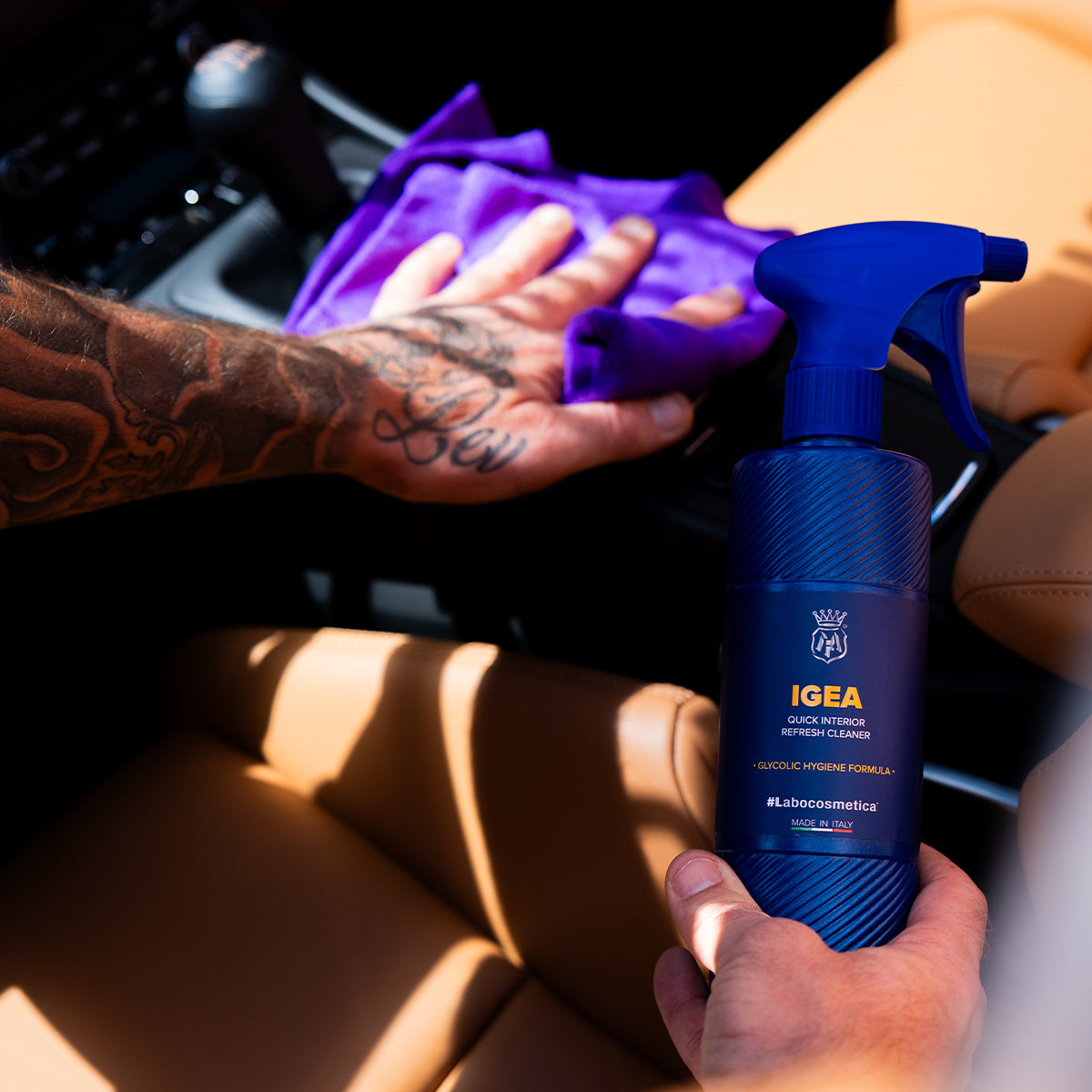 Person cleaning a car interior with a blue spray bottle labeled &#39;IGEA&#39; and a purple cloth.