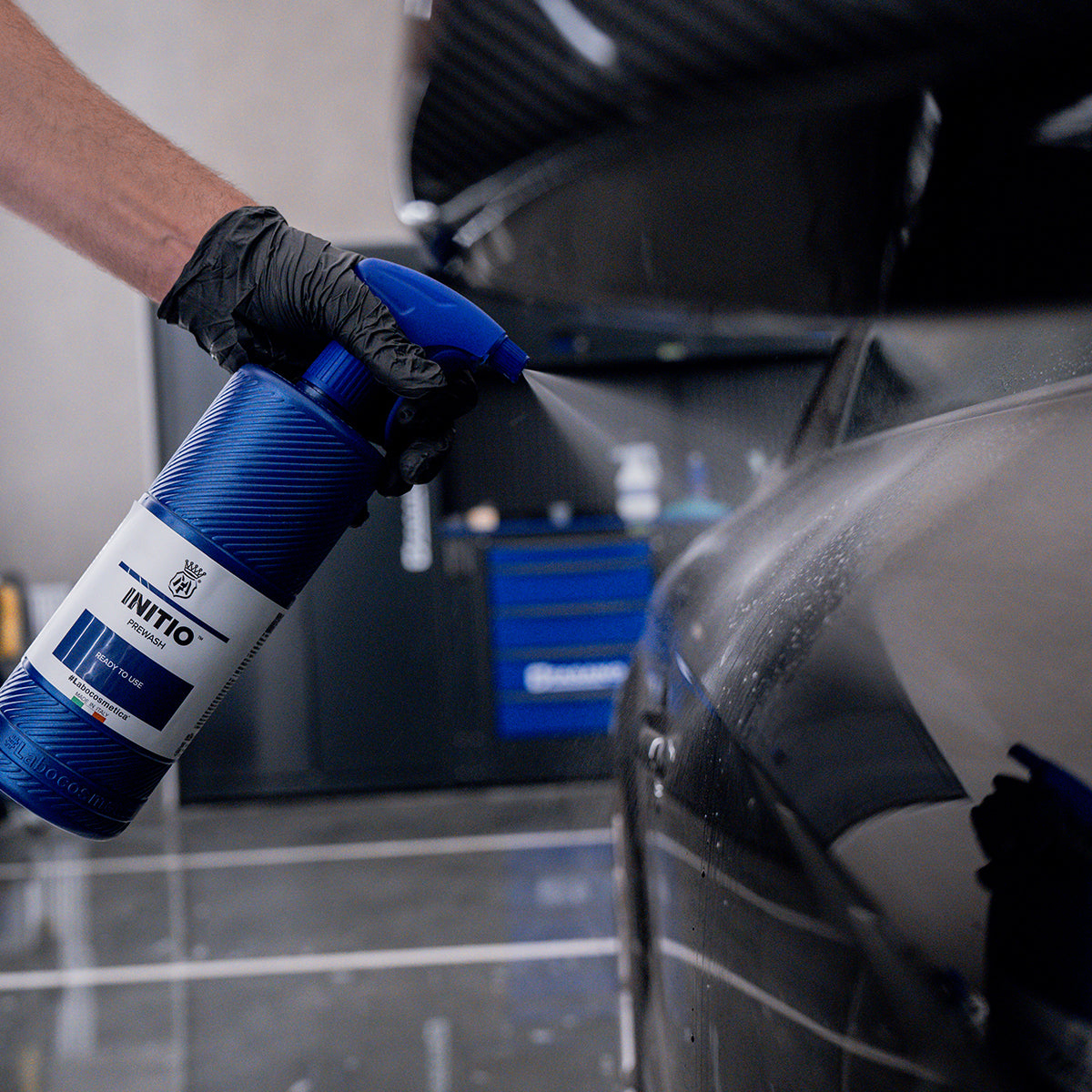 Person using a blue spray bottle labeled &#39;INITIO&#39; on a car in a garage.