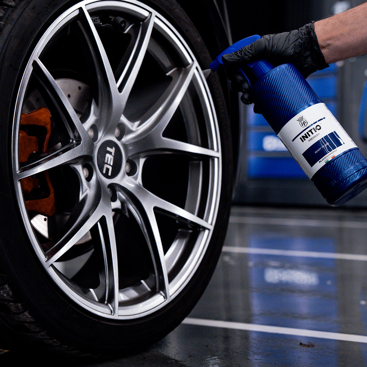 Person cleaning a car wheel with a blue spray bottle in a garage setting