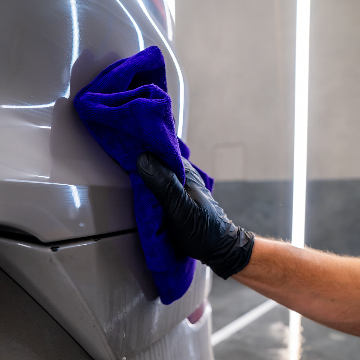 Person cleaning a car with a blue towel wearing black gloves
