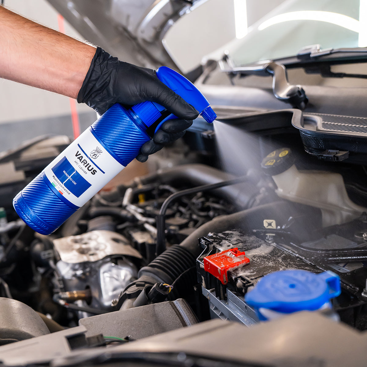 Person using a blue spray can labeled &#39;Varius&#39; on a car engine.