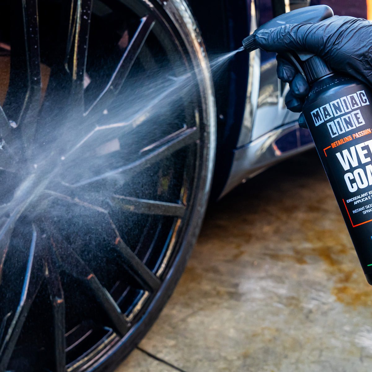 Person cleaning a car wheel with a spray bottle labeled &#39;Maniac Line Wet Coat&#39;.